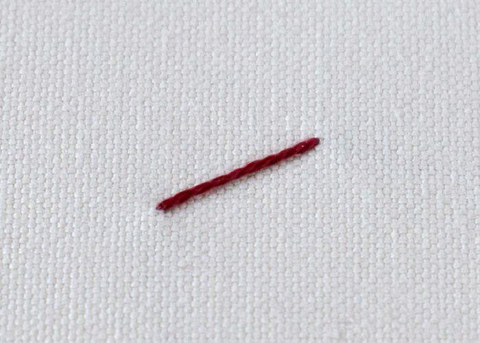 Un solo hilo rojo retorcido que reposa sobre un fondo de tela blanca texturizada.